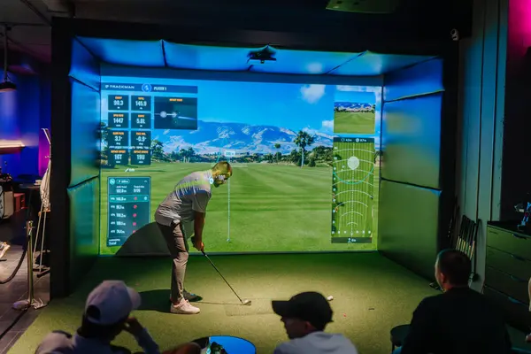Riga, Letonya - 8 Ocak 2024 - Kapalı alanda Trackman simülatörü kullanan bir golfçü, ekranda gösterilen sanal golf sahası ve performans ölçüleriyle topa vurmaya hazırlanıyor.