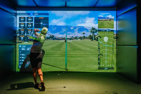 Riga, Letonya - 8 Ocak 2024 - İçerde Trackman simülatörü kullanan bir golfçü, ekranda yansıtılan sanal golf sahası ve performans ölçümleri ile bir salıncağı tamamlıyor.