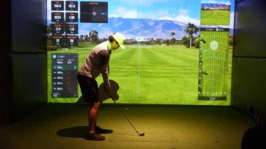 Riga, Letonya - 8 Ocak 2024 - İçerde Trackman simülatörü kullanan bir golfçü, ekranda sanal golf sahası ve performans verileri olan bir sopayı sallıyor.