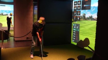 Riga, Letonya - 8 Ocak 2024 - İçerideki bir Trackman simülatöründe golf antrenmanı yapan bir kişi, sanal bir golf sahası ve performans verileriyle topa vurmaya hazırlanıyor.