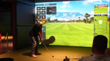 Riga, Letonya - 8 Ocak 2024 - İçerideki bir Trackman simülatöründe golf antrenmanı yapan bir kişi, sanal bir golf sahası ve performans verileriyle topa vurmaya hazırlanıyor.