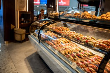 İstanbul, Türkiye - 21 Şubat 2020 - Arka planda müşterinin baktığı modern bir havaalanı kafe 'sinde içi taze sandviç, hamur işi ve fırınlanmış yiyeceklerle dolu bir vitrin