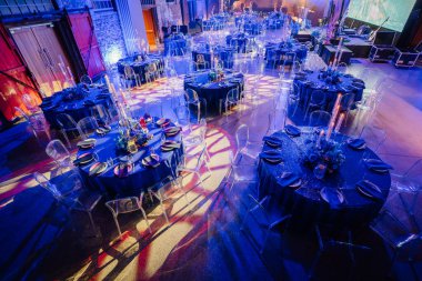 Yuvarlak masaları, mavi masa örtüleri, çiçekli süslemeleri, mumları ve renkli ışıklarla aydınlatılmış şeffaf sandalyeleri olan zarif ziyafet salonu..