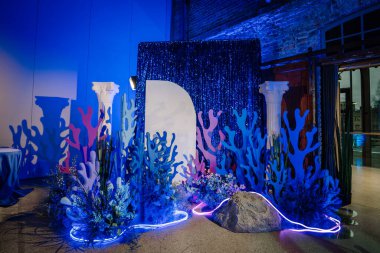 Riga, Latvia - January 11, 2025 - A decorative underwater-themed setup with colorful coral shapes, glowing neon lights, and a shimmering blue curtain backdrop indoors. clipart