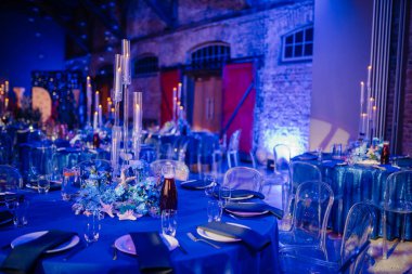 Mavi süslemeleri, mumları, cam sandalyeleri ve çiçekli süslemeleri olan zarif bir etkinlik masası..