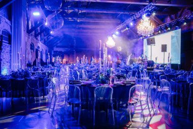 Zarif masa düzenine, cam koltuklara, avizelere ve mavi ışığa sahip müsrif etkinlik mekanı sofistike bir atmosfer yaratıyor..