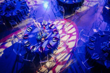 Dramatik ışıklandırma altında güzel dekore edilmiş bir yuvarlak masa manzarası çiçek süsü, mumlar ve zarif masa ayarları.