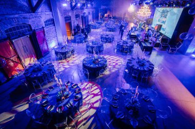 Riga, Letonya - 11 Ocak 2025 - Süslü yuvarlak masalar, zarif ışıklandırma ve ekranda Buz Diyarı 'nın yer aldığı büyük bir etkinlik salonunun genel görünümü