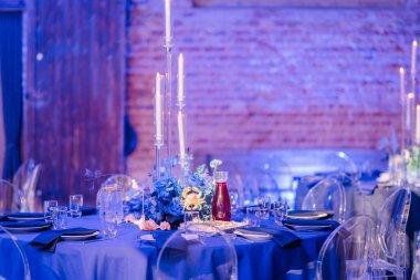 Mavi dekor, çiçek süsü, uzun mumlar, cam eşyalar ve tabaklar ile zarif bir masa..