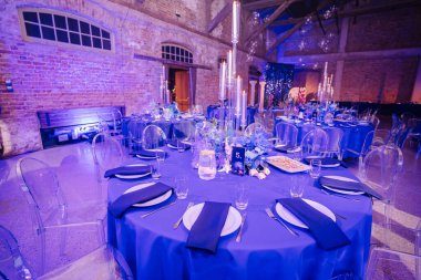 Mavi masa örtüsü, cam sandalyeler, mumlar, çiçek süsü ve dekore edilmiş bir yerde beş numaralı masa..