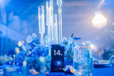 Riga, Letonya - 11 Ocak 2025 - Mavi çiçekli şık masa dekorasyonu, mum tutacağı ve resmi bir etkinlikte 14 numaralı masa, sakin ve sofistike bir ortam yaratıyor.