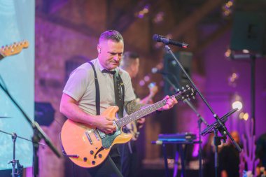 Riga, Letonya - 11 Ocak 2025 - Buz Diyarı temalı bir etkinlik sırasında canlı bir ışık ve canlı bir atmosferle bir gitarist tutkuyla sahnede performans sergiliyor.