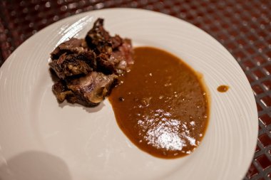 Belek, Turkey - February 25, 2020 - Close-up of a plate with roasted meat and rich brown sauce, served on a white dish, showcasing a simple yet elegant gourmet meal. clipart