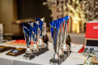 Belek, Türkiye - 27 Şubat 2020 - Resmi ödül töreninde plaketler, kitaplar ve şarap şişeleriyle dolu bir masada sergilenen parlak gümüş ve mavi ödüller.