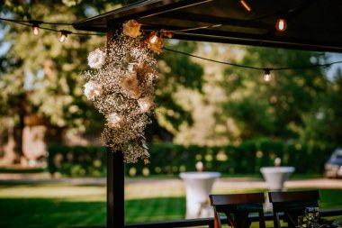 Close-up of floral decoration with white roses and babys breath on a gazebo, illuminated by string lights in a green outdoor setting clipart