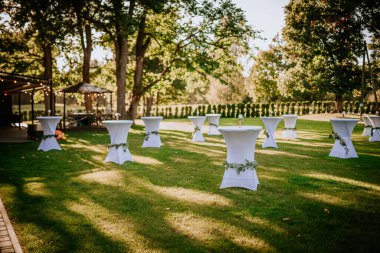 Beyaz örtülü açık hava kokteyl masaları, çiçek süslemeleri, ve manzaralı bir arka plan, düğünler ya da zarif etkinlikler için mükemmel..