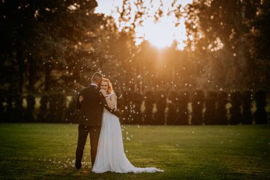 Gelin ve damat, baloncuklarla çevrili güneşli bir bahçede, düğünleri sırasında romantik ve huzurlu bir anı yakalıyorlar..