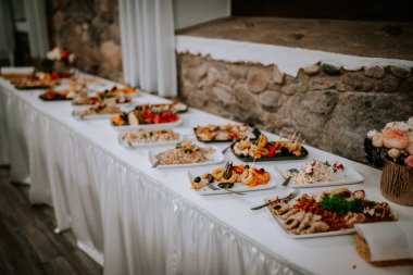 A long buffet table with assorted dishes, including seafood, salads, and appetizers, elegantly displayed on white tablecloths at an event. clipart