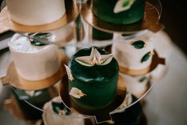 Çiçek süslemeli yeşil ve beyaz keklerin yakın plan çekimi, katmanlı bir stantta düzenlenmiş, karmaşık detaylar ve zarafet sergileniyor..