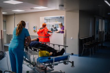 Valmiera, Letonya - 17 Ocak 2025 - Hastane resepsiyonunda bir hastaya sedyeyle yardım eden hemşire ve sağlık görevlisi. Bir resepsiyonist klinik ortamda çalışanlarla etkileşime geçer..