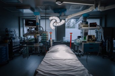 Valmiera, Latvia - January 17, 2025 - Dimly lit operating room with advanced medical equipment, surgical light, patient bed, monitors, and sterile tools, ready for procedures. clipart