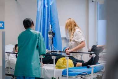 Valmiera, Letonya - 17 Ocak 2025 - Klinik bir ortamda tıbbi ekipman ve mavi perdelerle hastane yatağında yatan bir hastaya tıbbi personel.