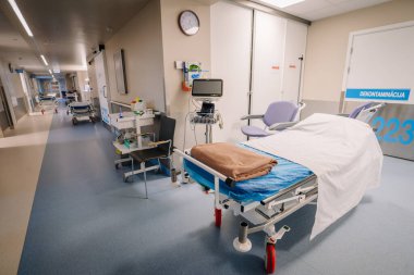 Valmiera, Letonya - 17 Ocak 2025 - Tıbbi yatağı, izleme ekipmanları, sandalyeleri ve malzemeleri olan temiz bir hastane koridoru. Sakin bir atmosferi olan parlak ve düzenli bir klinik ortam..