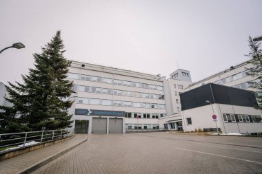 Valmiera, Letonya - 17 Ocak 2025 - Acil servis levhası, kaldırım yolu ve bulutlu bir gökyüzünün altındaki ağaçları çevreleyen modern bir hastane binası.