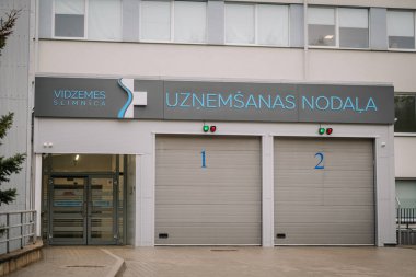 Valmiera, Letonya - 17 Ocak 2025 - 1 ve 2 etiketli iki garaj kapısı olan hastane acil servis girişinde modern tasarım ve açık tabela.