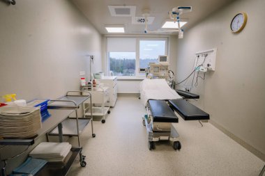 Valmiera, Letonya - 17 Ocak 2025 - Tıbbi gereçleri, ameliyat masası, steril çevre, depolama arabaları ve manzaralı bir penceresi olan modern bir hastane ameliyathanesi.