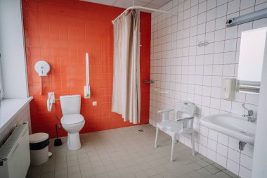 Valmiera, Letonya - 17 Ocak 2025 - Tuvaleti, lavabosu, banyosu, duşu, emniyet rayları, sandalyesi ve turuncu fayansları olan erişilebilir banyo, hareket sorunu olanlar için tasarlandı.