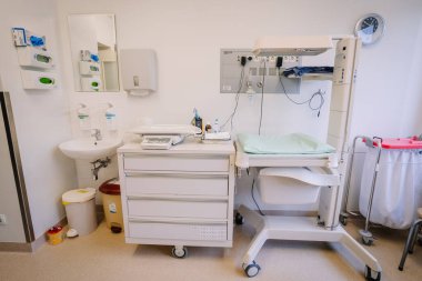 Valmiera, Letonya - 17 Ocak 2025 - Bebek bakım istasyonu, lavabosu, ölçeği, depolama çekmeceleri ve yeni doğan bakımı için temiz, düzenli bir sağlık ortamında ekipman bulunan tıbbi oda.