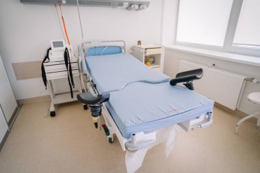Valmiera, Letonya - 17 Ocak 2025 - Doğum sırasında hasta bakımı için tasarlanmış temiz ve parlak bir odada tıbbi ekipmanla ayarlanabilir hastane yatağı.
