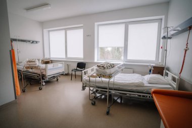 Valmiera, Letonya - 17 Ocak 2025 - İki yataklı hastane odası, bebek yatakları, sandalyeler, büyük pencereler ve tıbbi gereçler,.