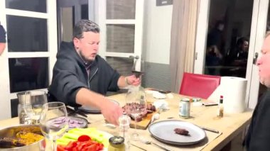 Sotogrande, İspanya - 25 Ocak 2024 - Bir grup insan ahşap bir masada ızgara yemek, sebze ve şarapla yemek yiyor..