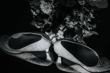 Valmiera, Letonya - 16 Ağustos 2024 - Aralarına bir alyans yerleştirilmiş, dramatik siyah-beyaz kompozisyonda bir çiçek buketiyle şekillendirilmiş dantelli gelinlik ayakkabıları.