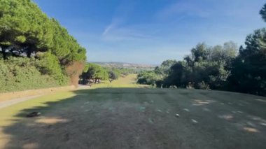 Sotogrande, İspanya - 26 Ocak 2024 - Güneşli bir günde açık mavi gökyüzü altında ağaçların manzaralı bir golf sahası, bir çim yolu ve bir kasaba.
