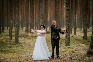 Valmiera, Letonya - 16 Ağustos 2024 - Gelin ve damat, uzun ağaçlarla çevrili, eğlenceli ve samimi bir düğün anı yaratan, eğlenceli bir parti patlatıcıları.