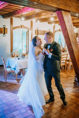 Valmiera, Latvia - August 16, 2024 - Bride and groom laughing joyfully while dancing indoors at their wedding reception, surrounded by decorated tables and warm lighting. clipart