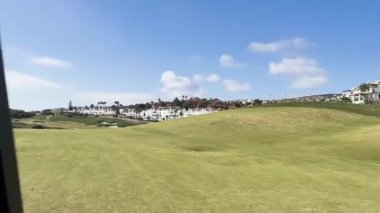 Sotogrande, İspanya - 26 Ocak 2024 - Güneşli bir günde açık mavi gökyüzüne karşı yeşil ve palmiye ağaçlarıyla çevrili modern beyaz binalar.