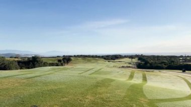 Sotogrande, İspanya - 26 Ocak 2024 - Geniş bir golf sahası, düzgünce budanmış yeşiller, kumdan sığınaklar, uzak dağlar, ve berrak mavi bir gökyüzü.