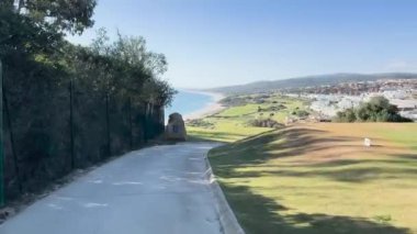 Sotogrande, İspanya - 26 Ocak 2024 - Okyanus manzaralı, kıyı şeridi, yeşillik ve hareket halindeki bir golf arabasından görülen uzak beyaz binalar.