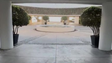 Sotogrande, İspanya - 26 Ocak 2024 - Çeşmesi, saksı ağaçları, modern mimarisi ve yumuşak gün ışığı altında uzak deniz manzaralı sakin bir avlu.