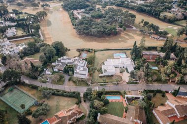 Sotogrande, İspanya - 26 Ocak 2025 - Yüzme havuzlu, tenis kortlu ve yeşilliklerle çevrili bahçeli lüks villaların havadan görünüşü. İHA atışı.