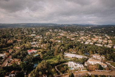 Sotogrande, İspanya - 26 Ocak 2025 - Lüks villaları, yüzme havuzları, ağaçları ve tepeleri olan, bulutlu bir gökyüzü altında sakin bir atmosfer yaratan yemyeşil bir yerleşim yeri manzarası.
