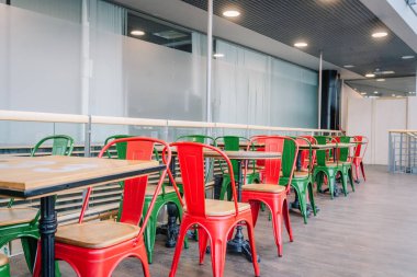 Riga, Latvia - January 24, 2025 - Modern indoor seating area with colorful red and green metal chairs and wooden tables on a hardwood floor, set in a bright open space. clipart