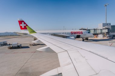 Malaga, Spain - January 24, 2025 - Airplane wing with airBaltic logo at an airport, showing a parked Swiss Airlines plane near a boarding gate under a clear blue sky. clipart