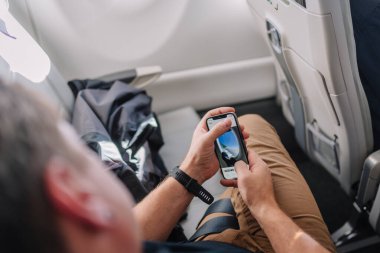 Riga, Letonya - 24 Ocak 2025 - Bir yolcu uçuşta otururken bir akıllı telefon kullanarak, modern seyahat alışkanlıklarını gösteren bir uçak kanadının penceresinden fotoğrafını çeker..