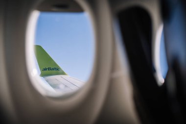 Riga, Letonya - 24 Ocak 2025 - Arka planda açık mavi bir gökyüzü ile bir uçak penceresine kuyruk sallayan bir hava Baltık uçağı görüntüsü