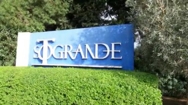 Sotogrande, İspanya - 26 Ocak 2025 - Açık havada güneşli bir günde yeşil çitler, ağaçlar ve yeşilliklerle çevrili Sotogrande yazılı mavi bir tabela.